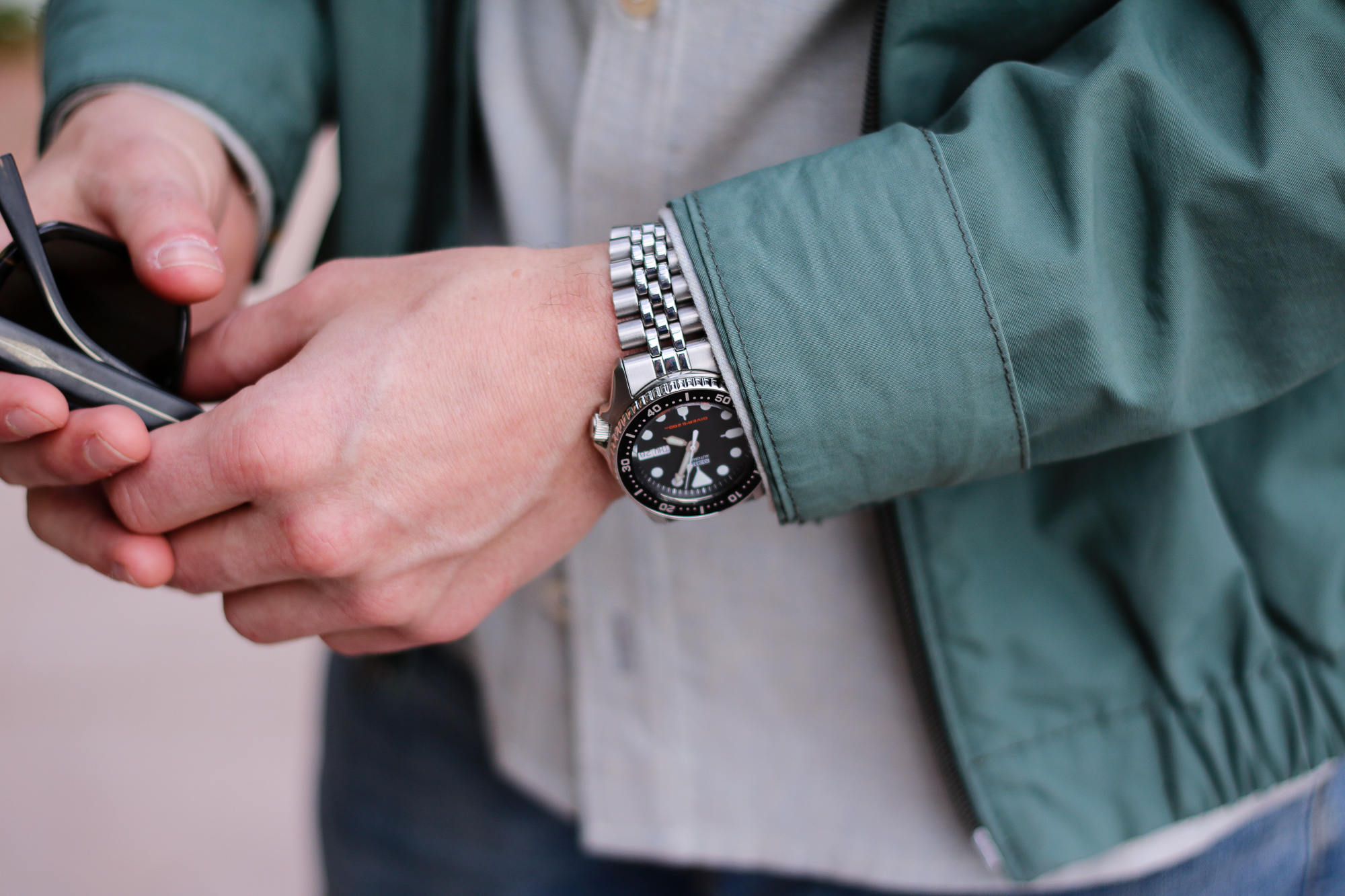 Someone holding sunglasses wearing a Seiko SKX013 dive watch with a stainless steel bracelet.